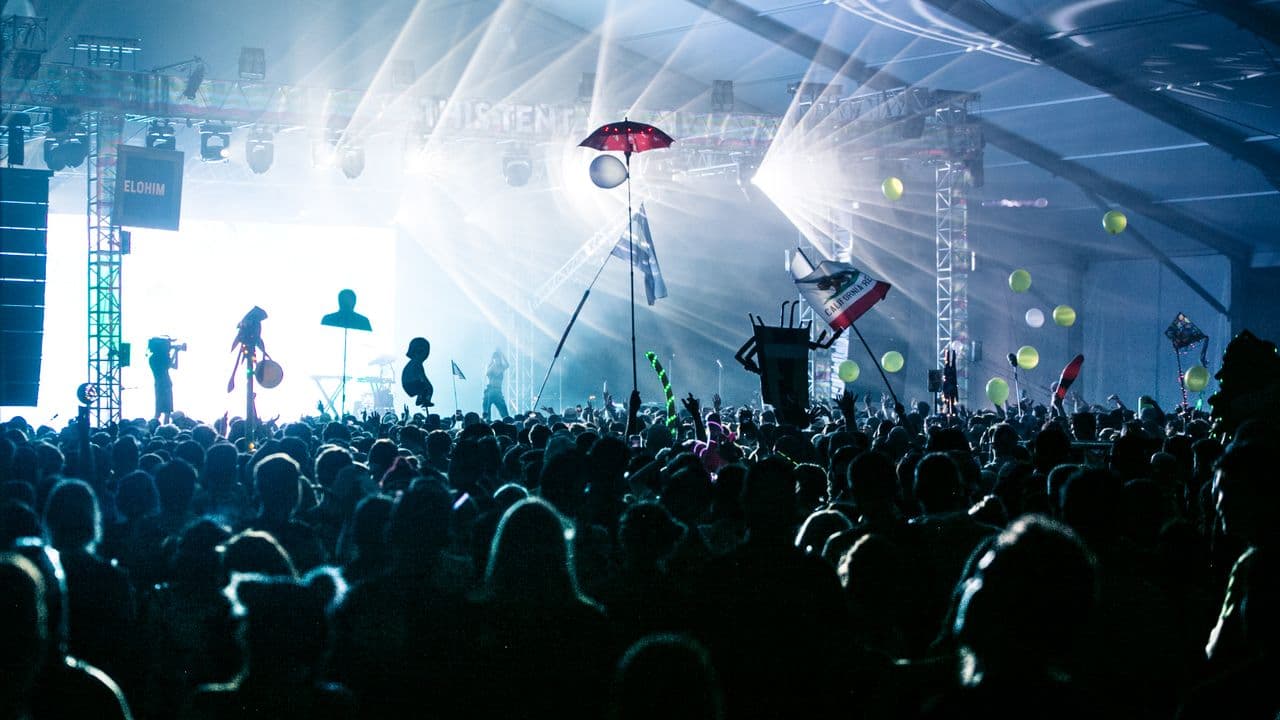 Vue sur une salle de concert plongée dans la pénombre, scène illuminée au fond.