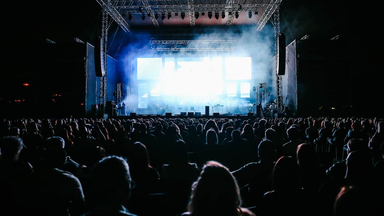 Spectateurs de dos face à une scène de concert baignée de lumière.