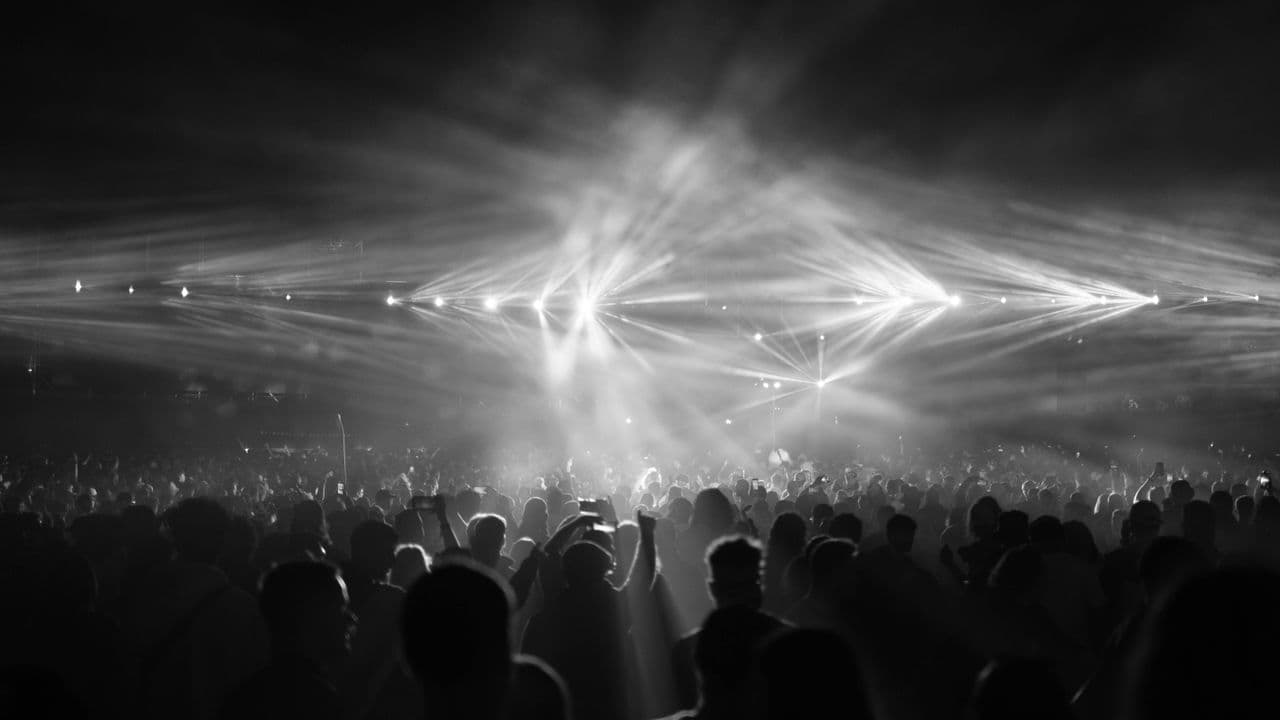Public levant les bras pendant un concert, dans une lumière colorée.
