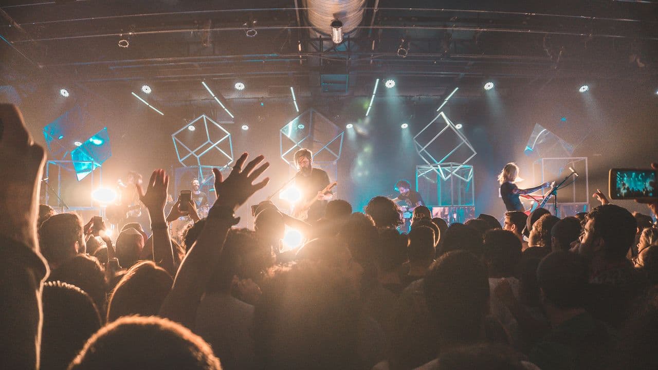 Spectateurs de dos face à une scène de concert baignée de lumière.