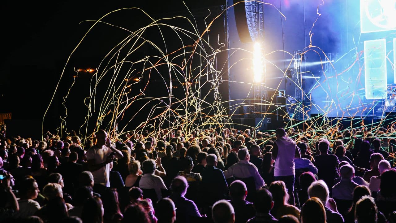 Ambiance de concert nocturne, faisceaux lumineux au-dessus du public.