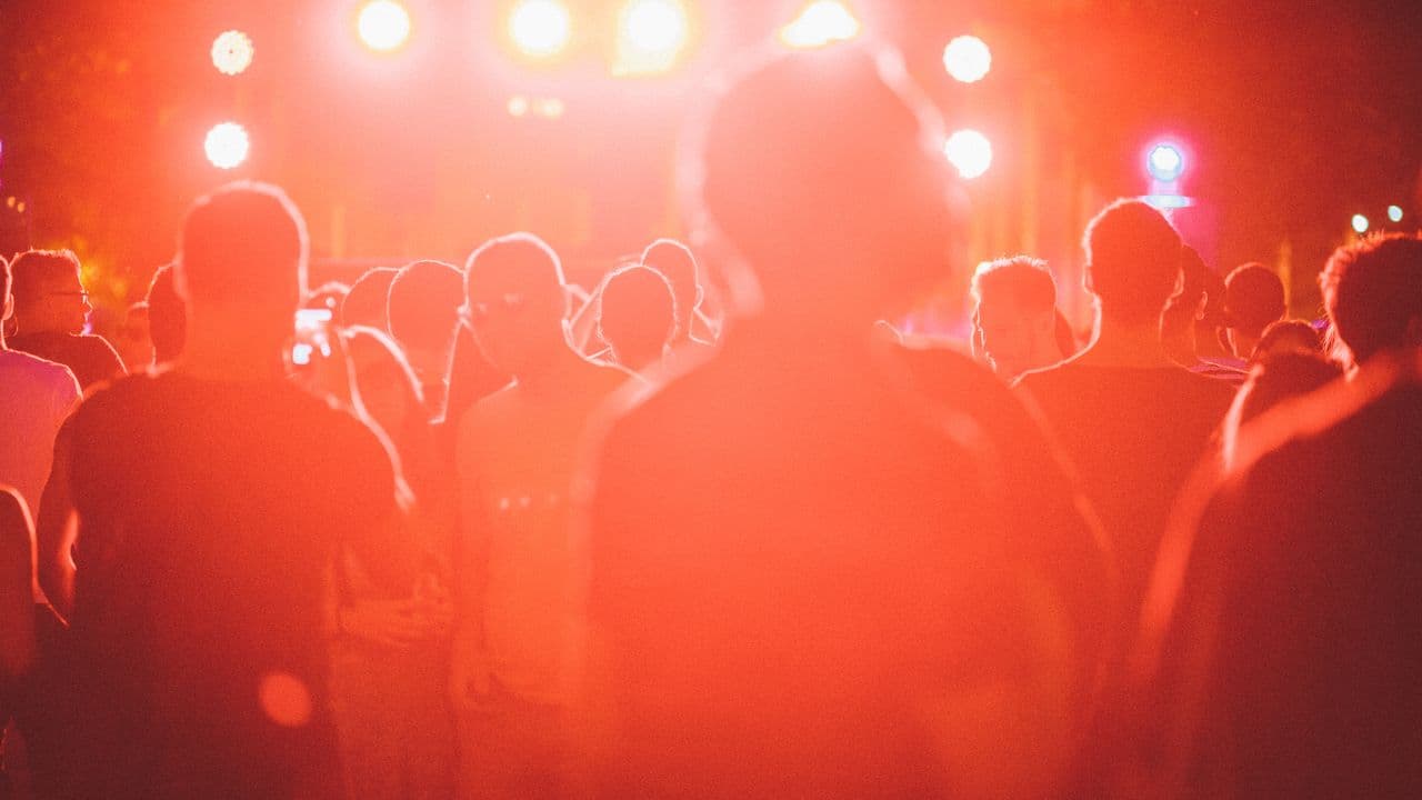 Scène de festival en extérieur au coucher du soleil, public au premier plan.
